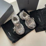 Sneakers Balenciaga bianche con dettagli riflettenti, confezionate in scatola minimalista e sacchetto nero elegante.