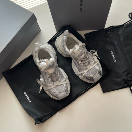 Sneakers Balenciaga bianche con dettagli riflettenti, confezionate in scatola minimalista e sacchetto nero elegante.