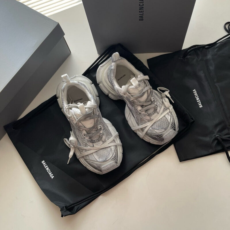 Sneakers Balenciaga bianche con dettagli riflettenti, confezionate in scatola minimalista e sacchetto nero elegante.