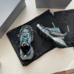 Scarpe sportive eleganti nere e grigie con dettagli teal, presentate su borsa raffinata e scatole minimaliste.