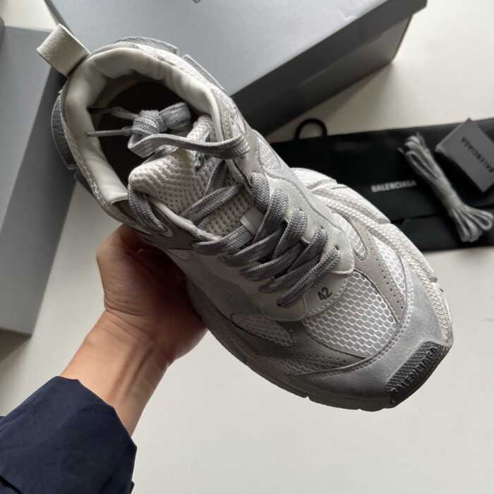 Scarpa sportiva grigia dettagliata con logo, tra scatola e elementi di presentazione moderna.