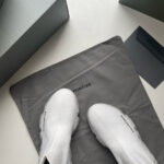 Sneakers minimaliste di lusso con scatola elegante e sacchetto protettivo in un packaging raffinato.