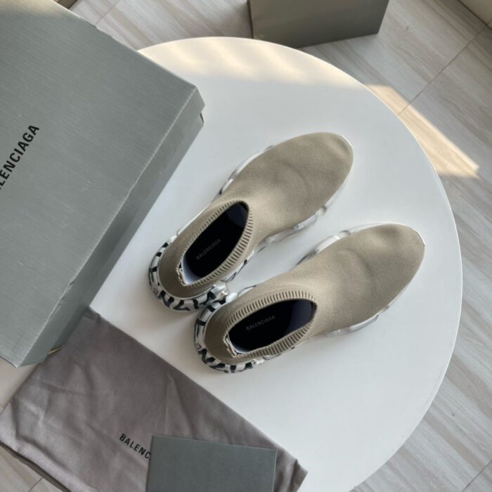 Sneakers Balenciaga nere e beige su tavolo bianco con scatole e dust bag di lusso.
