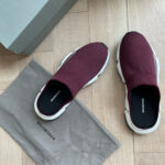 Scarpe Balenciaga eleganti in burgundy con dust bag e scatola moderna su pavimento in legno.