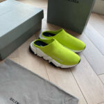 Scarpe slip-on verdi lime Balenciaga con scatole di lusso e borsa elegante in ambientazione moderna.