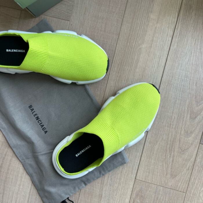 Sneaker neon Balenciaga su pavimento in legno con custodia grigia.