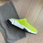Sneaker neon gialla Balenciaga su pavimento in legno, stile minimalista e bag dustbag inclusa.