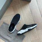Scarpe Balenciaga minimaliste in bianco e nero su pavimento in legno, stile moderno e di lusso.