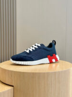 Scarpa sneaker navy con dettagli rosso e bianco su supporto di legno, stile minimalista.