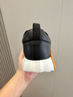 Sneaker nera moderna con suola bianca e dettagli arancioni, design sportivo ed elegante.