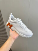 Sneaker bianca moderna con suola texturizzata e dettaglio arancione sul tallone.