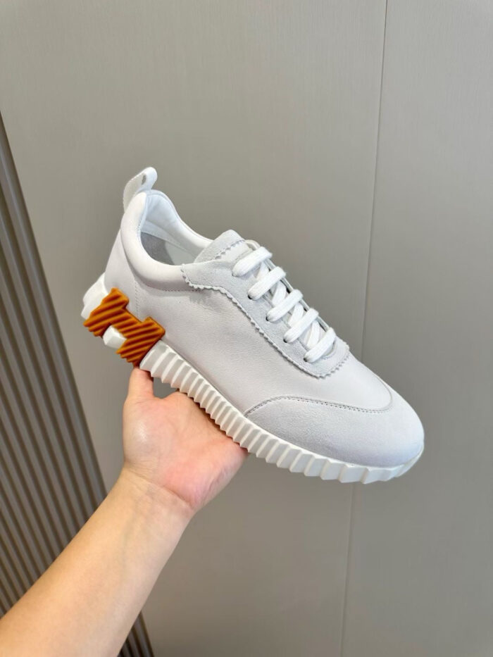Sneaker bianca moderna con suola texturizzata e dettaglio arancione sul tallone.