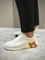 Sneaker bianca moderna con dettaglio arancione, pantaloni slim neri e design elegante e versatile.