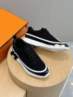 Sneakers di lusso nere con dettagli bianchi, elegante display su supporto in legno e box arancione.