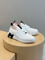Sneakers bianche moderne con dettagli neri e arancioni, pure su pedana di stile minimalista.