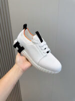 Sneaker bianca moderna con dettagli arancioni, suola antiscivolo e design minimalista.