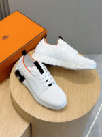 Sneakers bianche moderne con dettagli nero e arancione, display su pedestal con scatola orange.