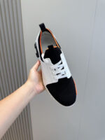 Sneaker moderna nero, bianco con dettagli arancioni, leggera e versatile per sport e casual.