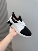 Sneaker moderna bianca e nera con dettagli arancioni, stile casual e design sportivo.