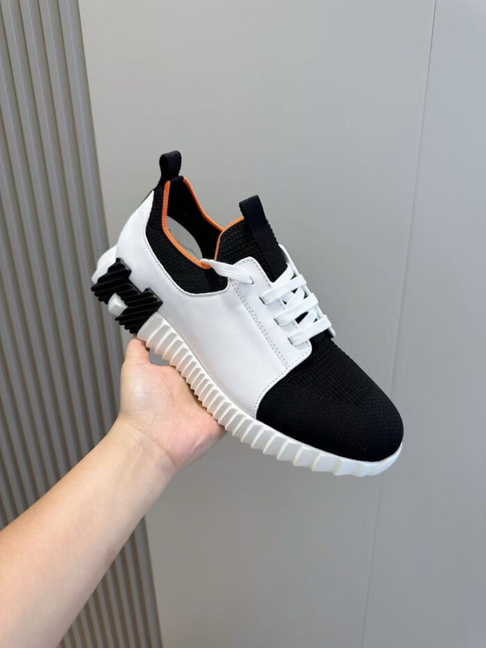 Sneaker moderna bianca e nera con dettagli arancioni, stile casual e design sportivo.