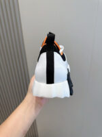 Sneaker bianca con dettagli nero e arancio, suola robusta e design sportivo moderno.