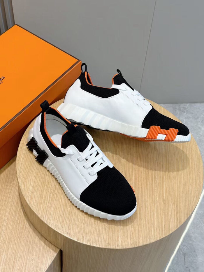 Sneakers moderne nero e bianco con dettagli arancioni, su piedistallo in legno, stile e comfort garantiti.