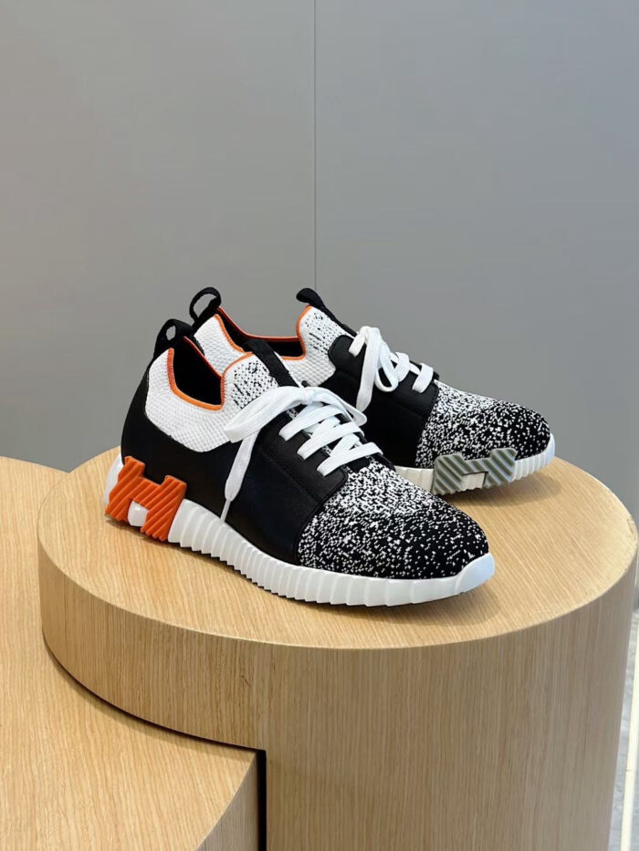 Sneakers moderne con dettagli speckled, accenti arancioni e design innovativo su pedale di legno.