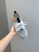 Sneaker sportiva grigia con dettagli arancioni e bianchi, leggera e moderna per atletismo e casual.