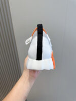 Sneaker bianca moderna con dettagli neri e arancioni, tenuta in mano, stile athleisure.