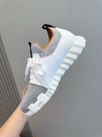 Sneaker bianca moderna con suola chunky, dettagli grigio e arancione, stile casual e sportivo.