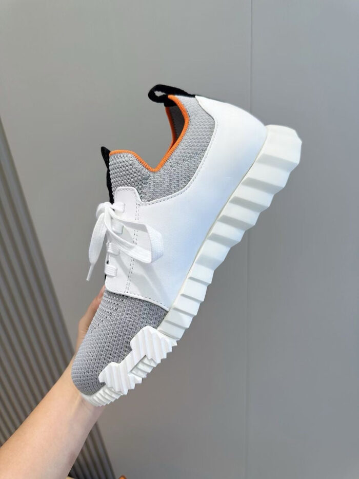 Sneaker bianca moderna con suola chunky, dettagli grigio e arancione, stile casual e sportivo.
