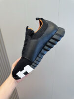 Sneaker moderna nero e bianco con dettagli arancioni e suola robusta dal design futuristico.