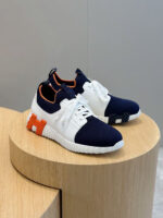Sneakers moderne blu, bianco e arancione su pedana in legno, stile casual e sportivo.