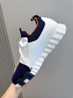 Sneaker moderna con dettagli arancioni, suola texturizzata e design sportivo in bianco e blu.