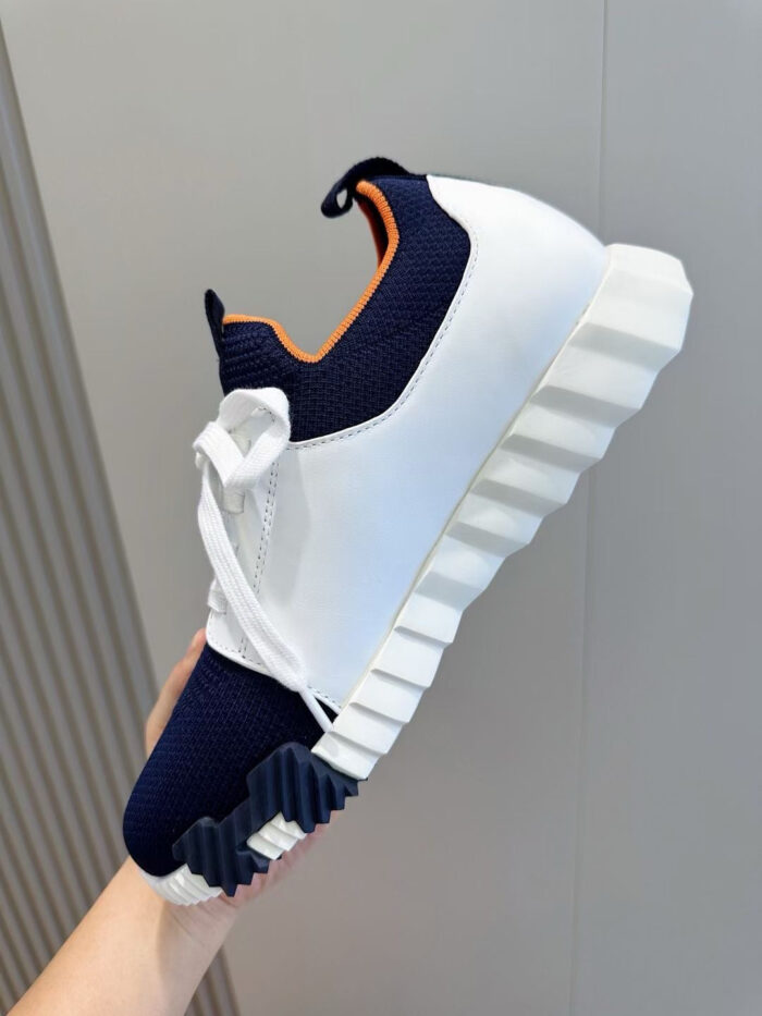 Sneaker moderna con dettagli arancioni, suola texturizzata e design sportivo in bianco e blu.