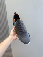 Scarpa sportive grigia con dettagli arancioni, suola bianca e design moderno for men or women.