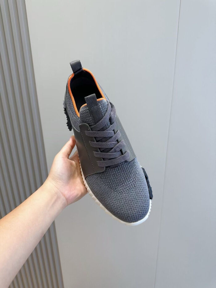 Scarpa sportive grigia con dettagli arancioni, suola bianca e design moderno for men or women.