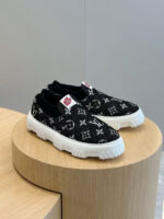 Scarpe slip-on Louis Vuitton monogram in tessuto nero, su supporto in legno elegante.