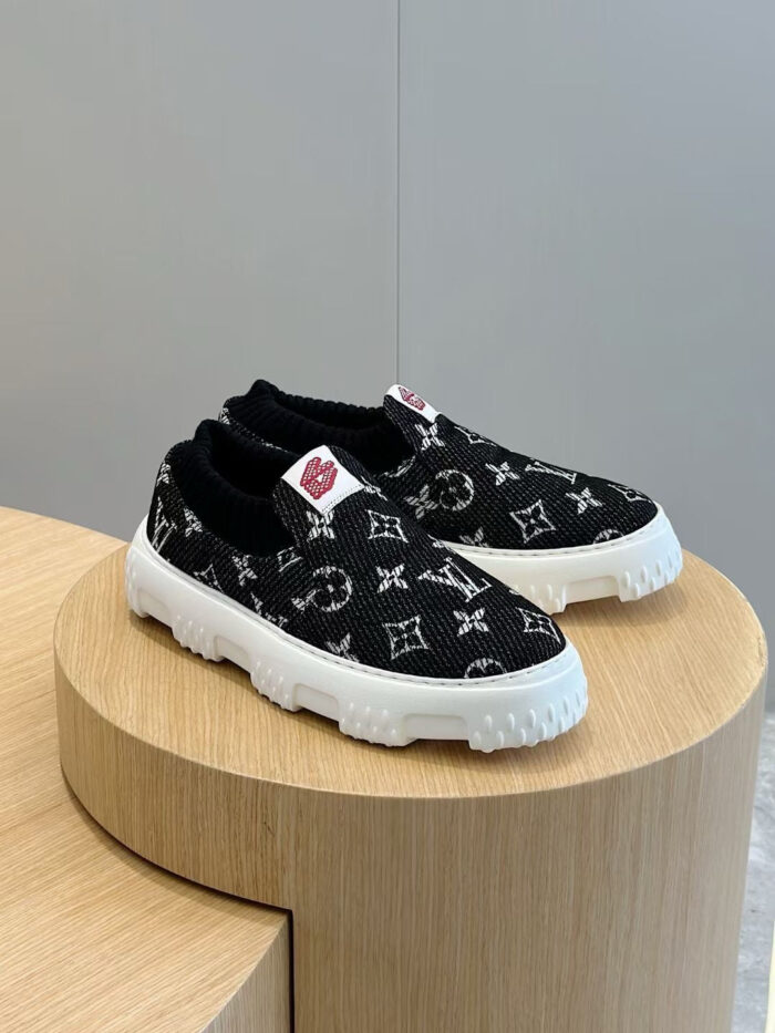 Scarpe slip-on Louis Vuitton monogram in tessuto nero, su supporto in legno elegante.