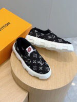 Scarpe slip-on di lusso nere con suola bianca e packaging arancione, stile elegante e moderno.
