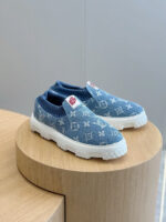 Scarpe slip-on in denim blu con logo, su piedistallo in legno, stile casual e di lusso.