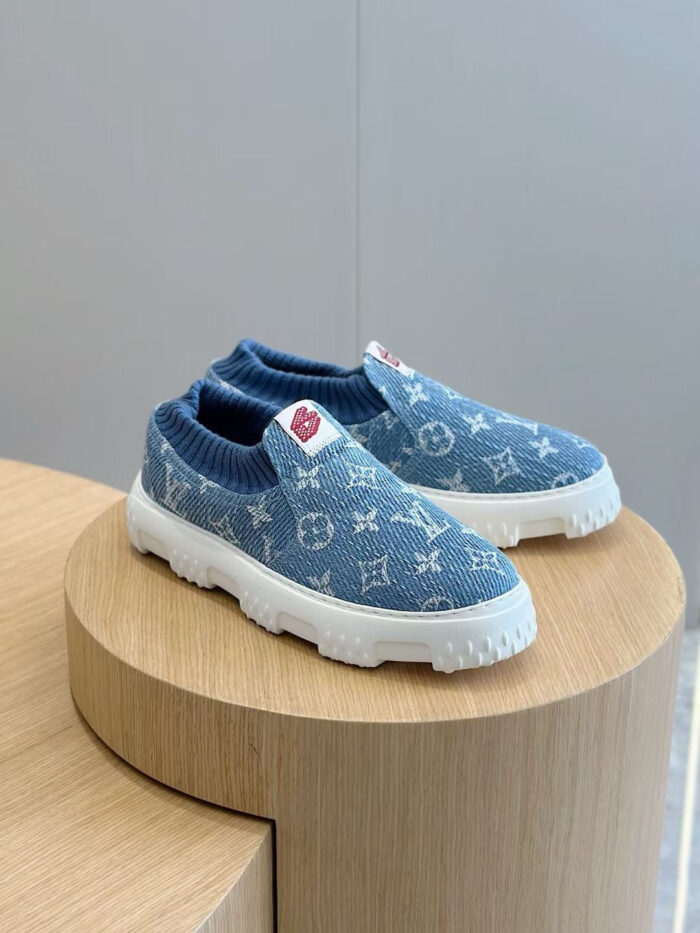 Scarpe slip-on in denim blu con logo, su piedistallo in legno, stile casual e di lusso.