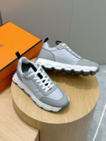 Sneakers moderne grigie con suola bianca, display in legno e box arancio, stile elegante.