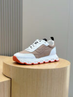 Sneaker moderna con suola arancione, design sporty e dettagli eleganti su pedestal di legno.