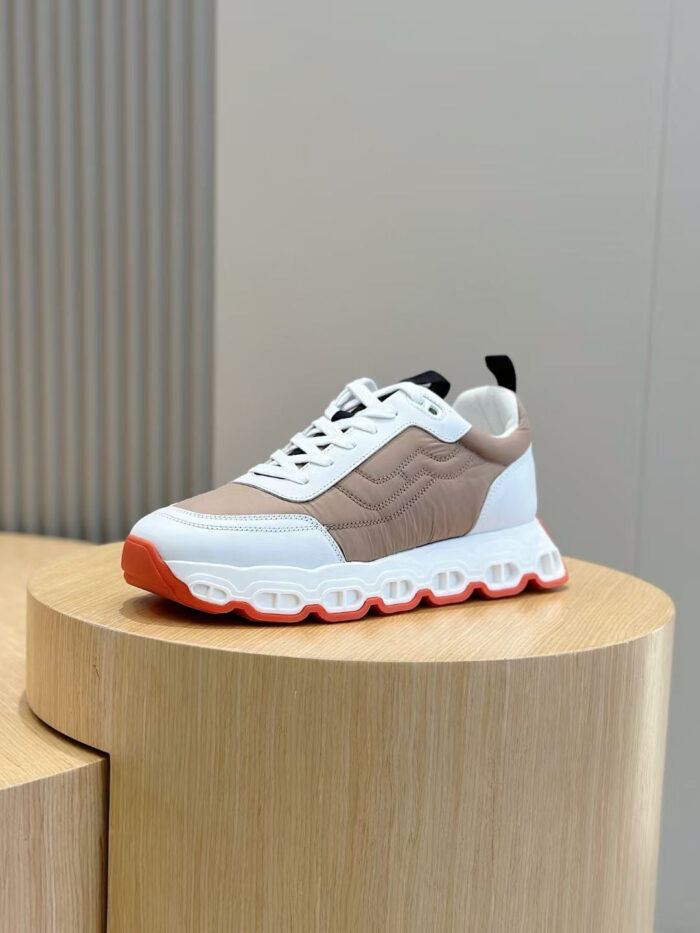 Sneaker moderna con suola arancione, design sporty e dettagli eleganti su pedestal di legno.