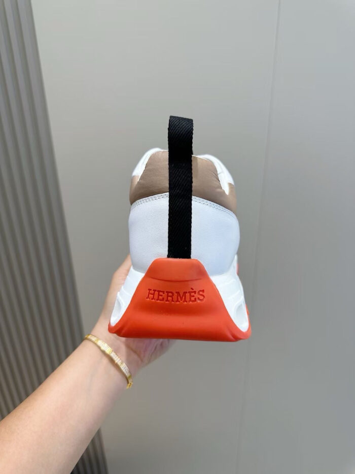 Sneaker Hermès bianca con dettagli arancioni e logo sul tallone, eleganza e stile contemporaneo.
