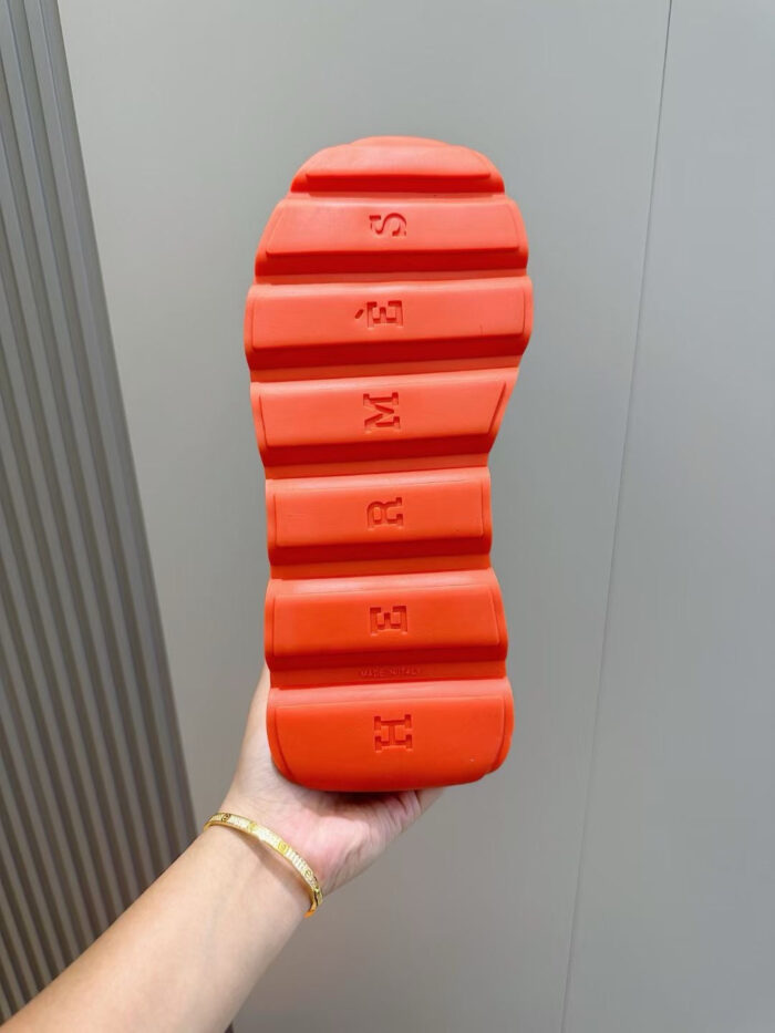 Sola di sneaker sportiva arancione, design moderno e dettagli segmentati, vista ravvicinata con mano.