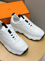 Sneaker bianche moderne con dettagli eleganti, su superficie di legno con box arancione sullo sfondo.