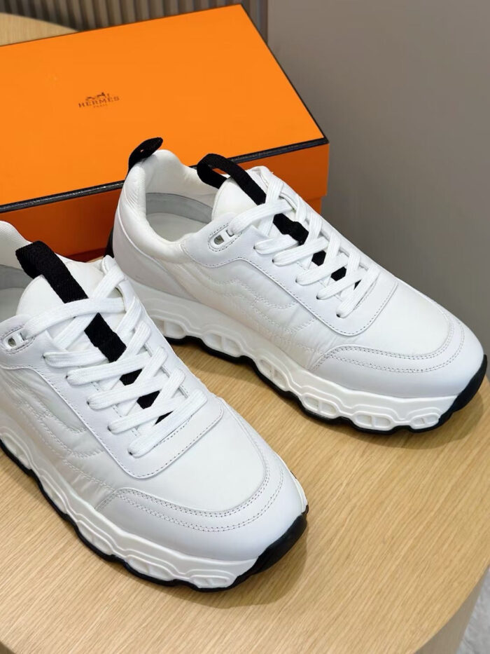 Sneaker bianche moderne con dettagli eleganti, su superficie di legno con box arancione sullo sfondo.