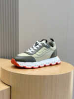 Sneaker moderna in verde, beige e arancione, su supporto di legno su sfondo minimalista.